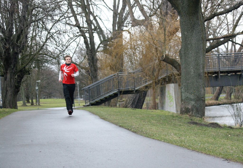 Ein Mann in Jogging-Kleidung läuft in einem Park. Die Natur um ihn herum ist winterlich kahl.