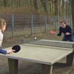 An einer Tischtennisplatte im Park spielen eine Frau und ein Mann.