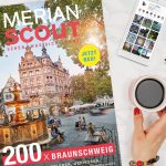 Das Heft MERIAN Scout Braunschweig liegt auf einem Tisch, daneben eine Hand, die einen Kaffee hält, ein Handy und ein Notizblock.