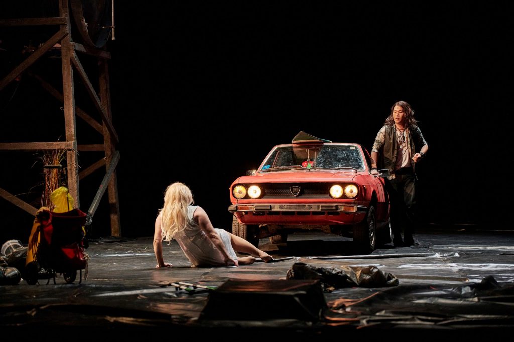 Zwei Menschen neben einem Auto auf einer Bühne.