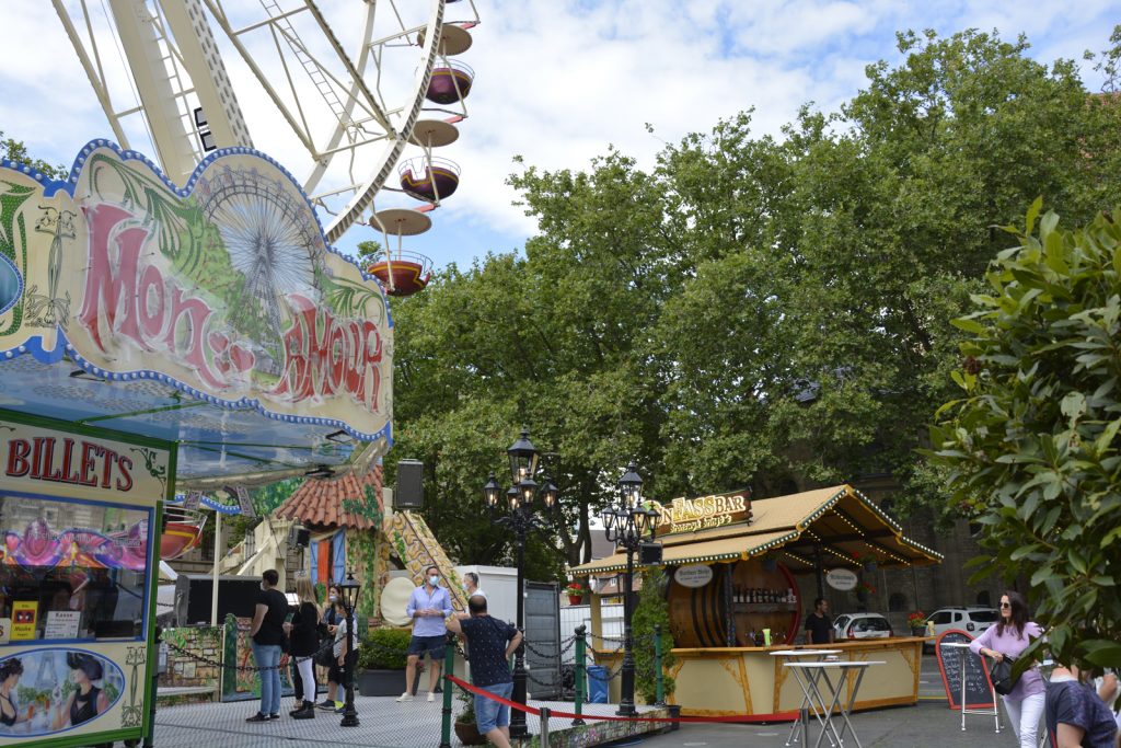 Im Hintergrund ein Imbissstand. Links im Bild ist das Riesenrad mit seinem Kassenhäuschen zu sehen.