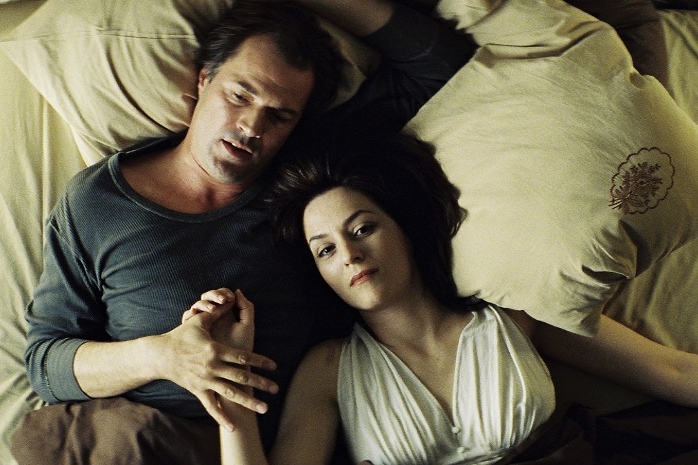 Filmstill aus dem Film Das Leben der Anderen: Ein Mann und eine Frau liegen in einem Bett und halten Händchen.