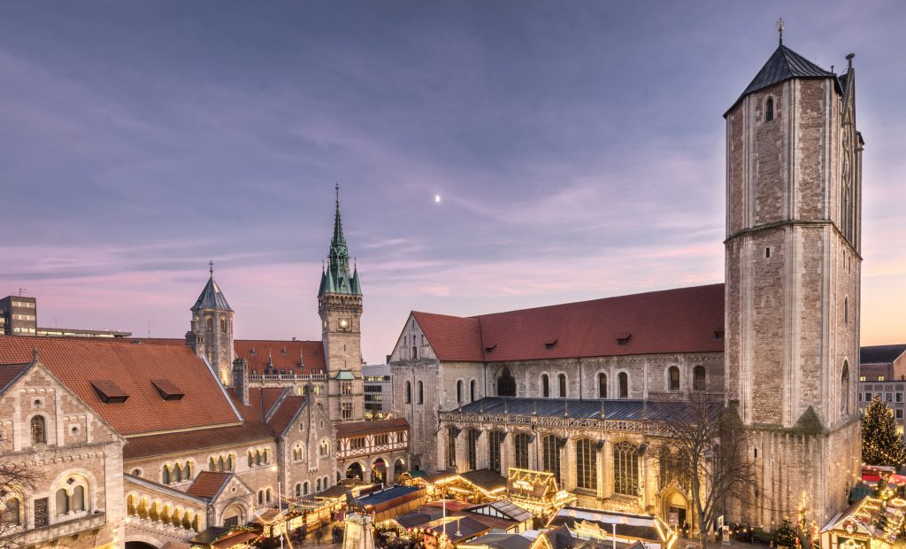 Überblick über den Braunschweiger Weihnachtsmarkt. Im Hintergrund sieht man den rechten Teil der Burg Dankwarderode, den Rathausturm sowie rechts im Bild den Dom. Dazwischen stehen festlich beleuchtete Buden.