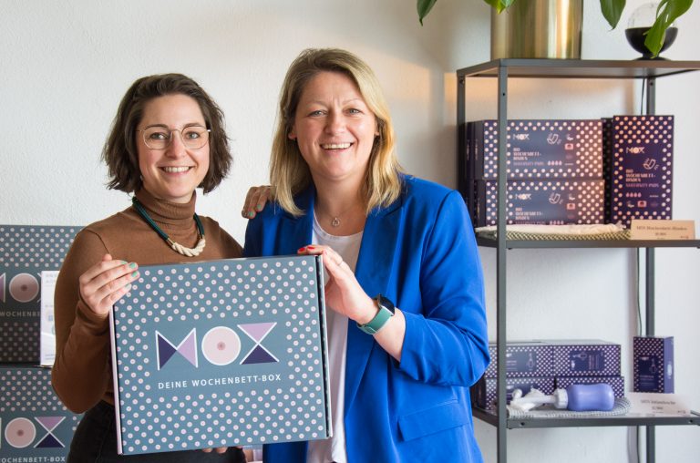 Zwei Frauen halten eine Box mit der Aufschrift "MOX" in der Hand