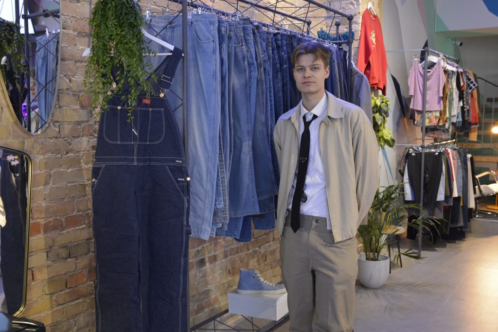 Junger Mann vor einer Kleiderstange im Vintage-Laden.