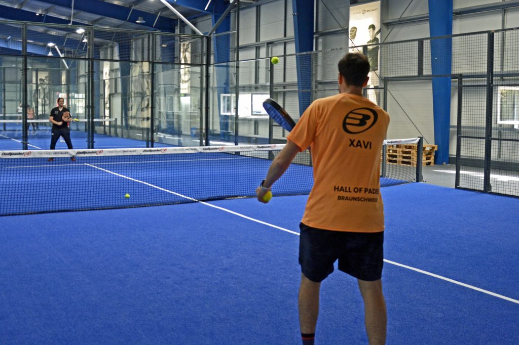 In einer Padel-Tennis Anlage steht ein Trainer mit dem Rücken zum Betrachter.