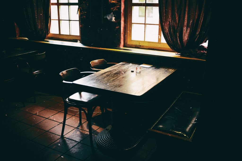 Ein Tisch in einer dunklen Kneipe, der vom einfallenden Licht des Fenster erhellt wird.