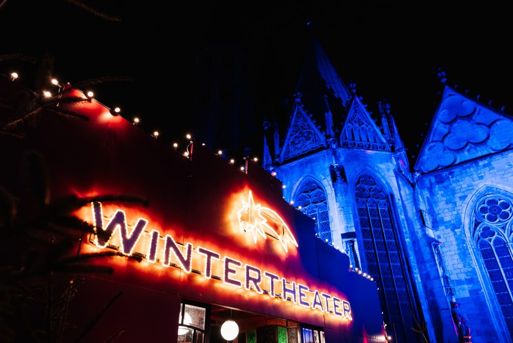 Leuchtender Schriftzug Wintertheater mit beleuchteter Kirche im Hintergrund
