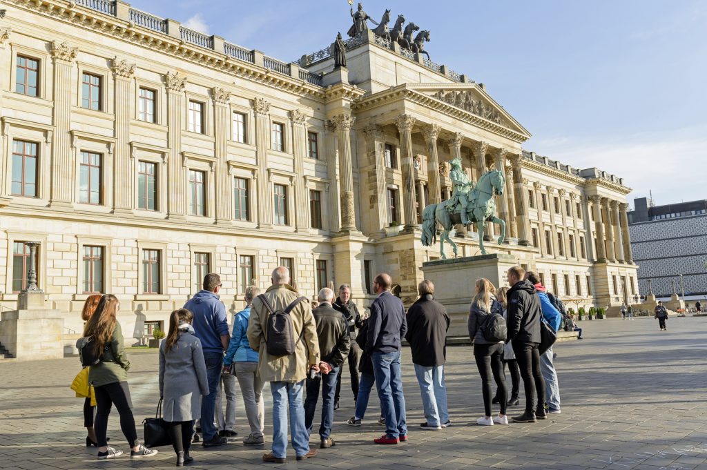Eine Menschengruppe steht vor dem Schloss in Braunschweig.